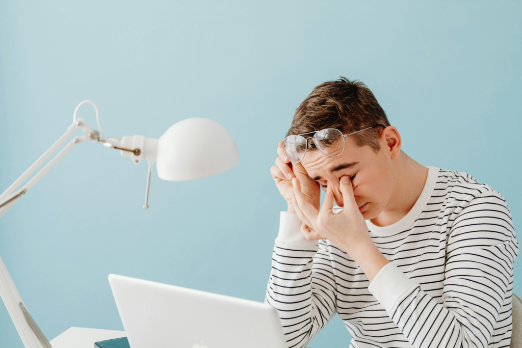 Tired man rubbing his eyes while working on a laptop, showing symptoms of digital eye strain and computer vision syndrome