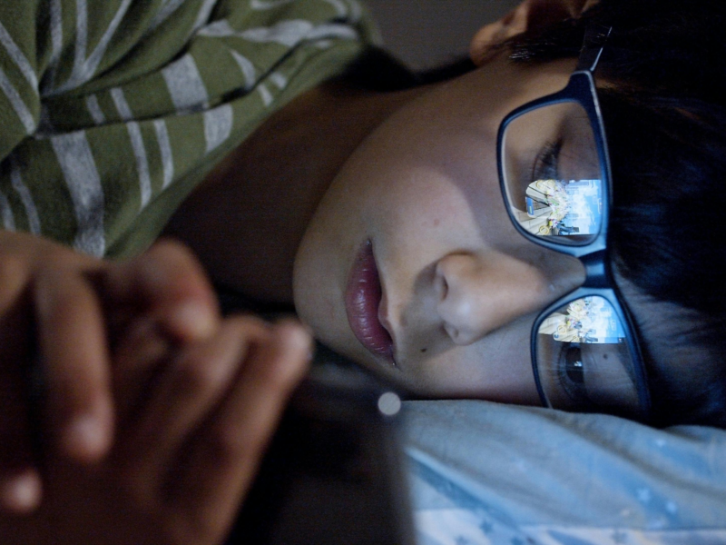 Child looking at a smartphone in dim lighting, symbolizing modern screen exposure and its effects on vision