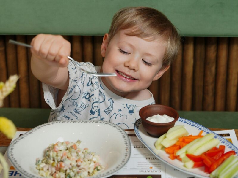 A smiling child enjoying a healthy meal rich in colorful vegetables and fish, representing nutrition for eye health.