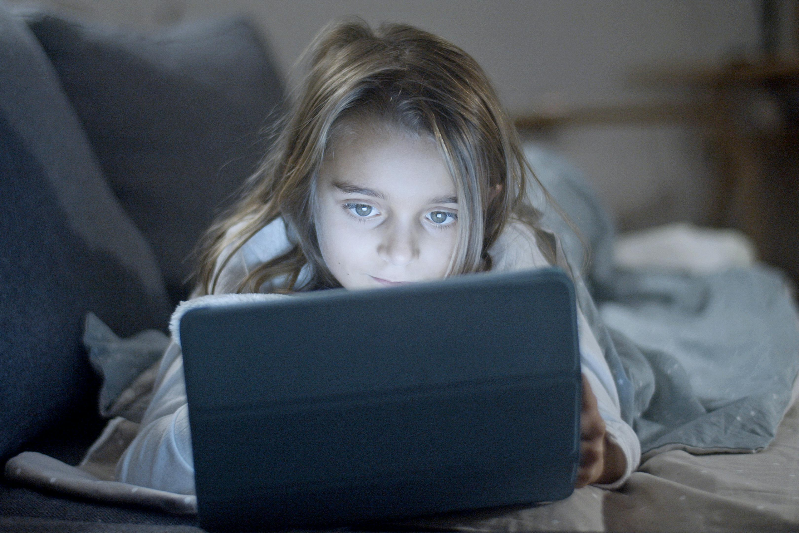 The negative impact of screen time and childrens sleep showing a child using a phone in a dark bedroom.