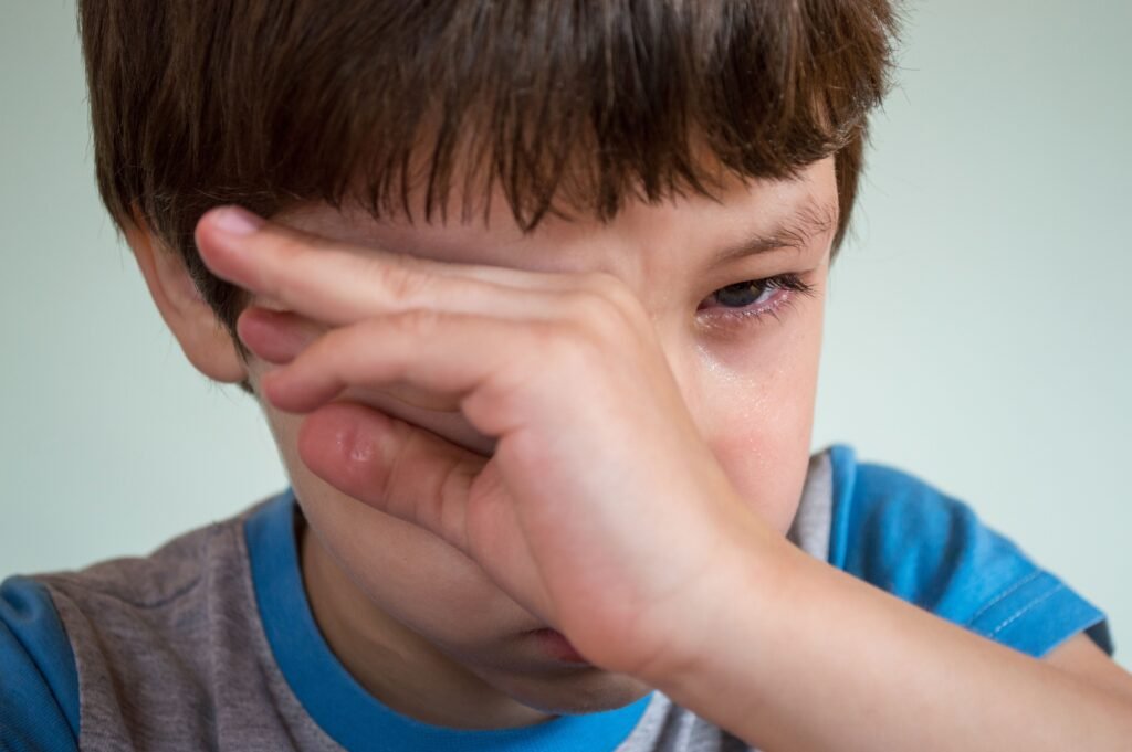 A tired child rubbing eyes from screen fatigue, illustrating common issues in children eye health.